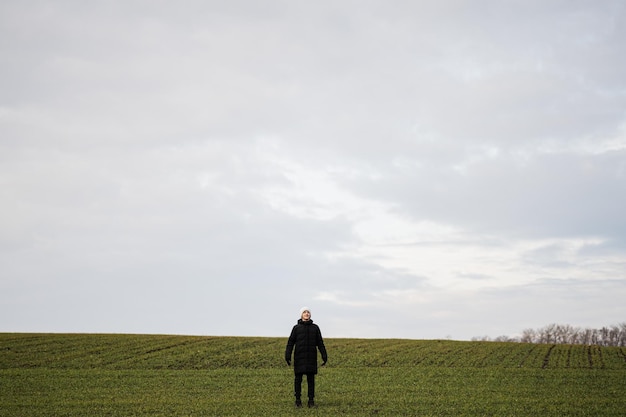 Teen boy wearing black jacket and white hat outside enjoys in the early spring field