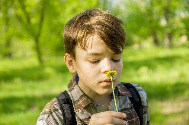 タンポポの花を持つ十代の少年ポートレート クローズ アップぼやけて緑の背景屋外