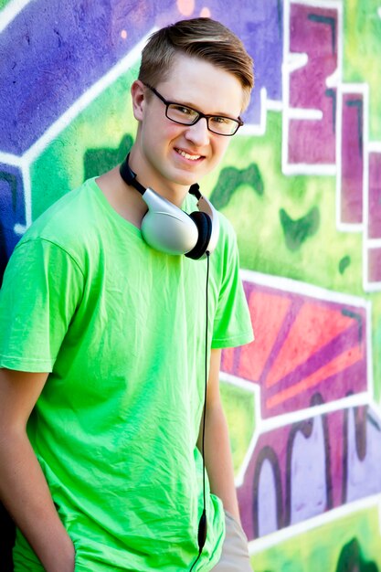 Foto ragazzo teenager con gli auricolari vicino al muro di graffiti.