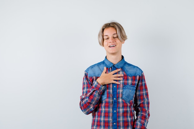 Teen boy with hand on chest in checkered shirt and looking pleased. front view.