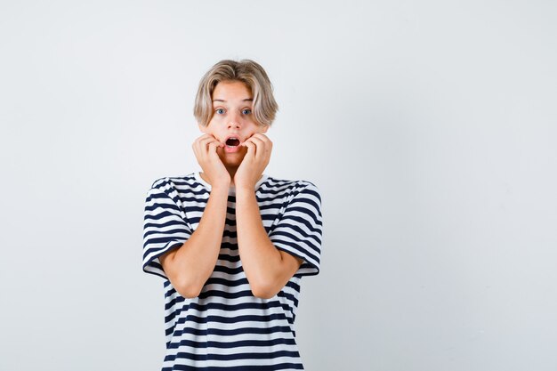 Teen boy with hands on cheek, opening mouth in t-shirt and looking horrified . front view.