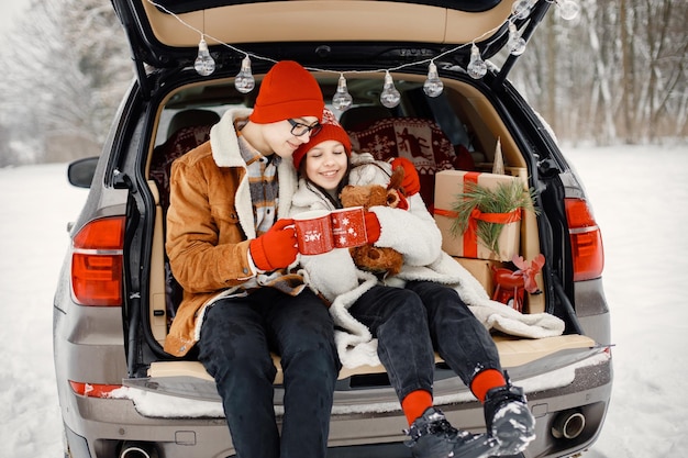 Брат и сестра-подросток сидят в багажнике открытой машины в зимнем парке