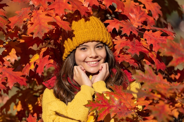 秋の紅葉の十代の子供の女の子は、自然な背景に秋の葉で帽子の陽気な十代の子供を背景に残します