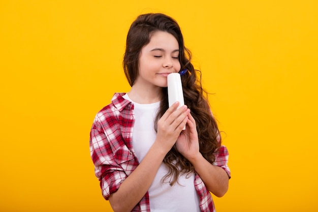 Photo teen child girl with shampoo bottle or shower gel isolated on yellow background kids hair cosmetic product