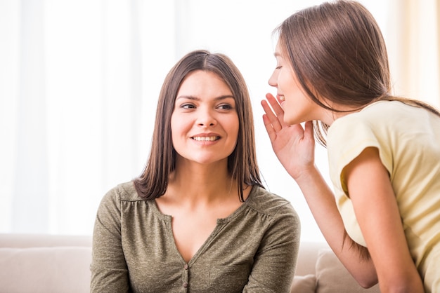 La figlia teenager sta bisbigliando qualcosa a sua madre.