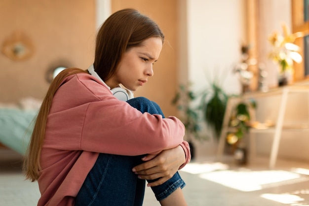 Concetto di depressione adolescenziale ragazza adolescente stressata seduta sul pavimento della sua camera da letto che guarda in basso sentendosi sconvolta e sola