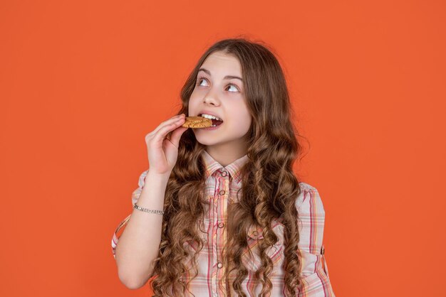 10 代の少女がオレンジ色の背景にオートミール クッキーをかむ