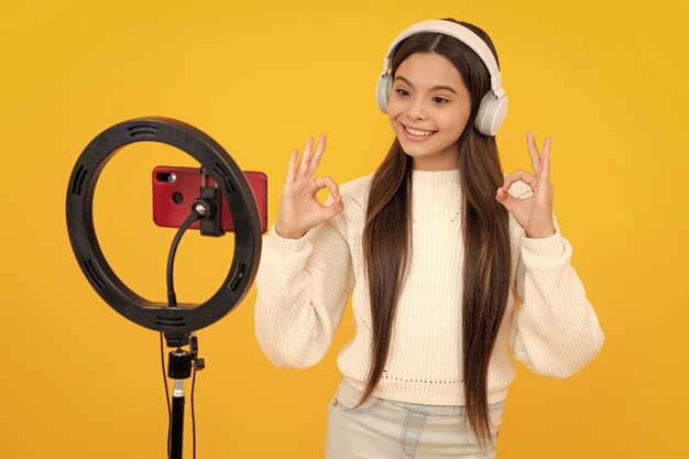 10 代の少女ブロガーのインフルエンサーは、オンライン ビデオを作成するために三脚に自撮り LED ランプとスマートフォンを使用します。