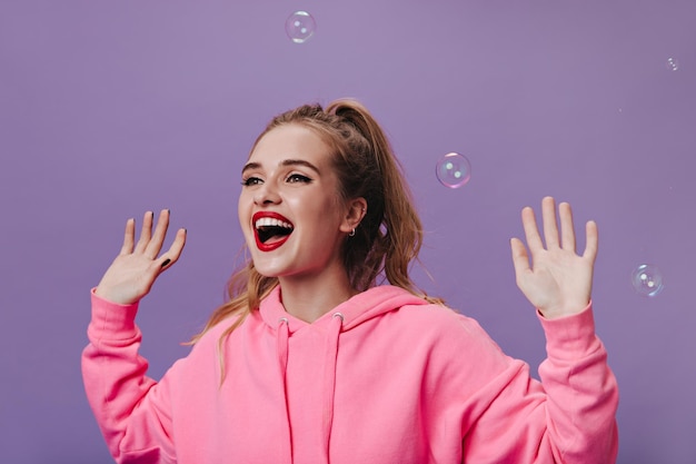 泡と紫色の背景に笑みを浮かべて明るいピンクのパーカーの十代の少女孤立した背景で笑ってスウェットシャツの幸せな女