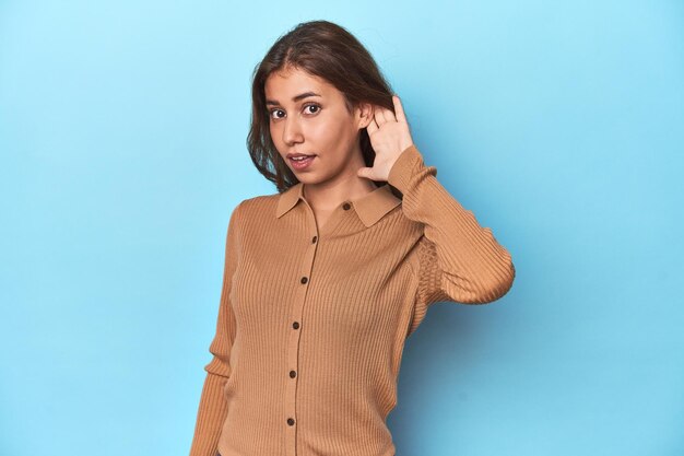 Teen girl in brown polo shirt on blue trying to listening a gossip