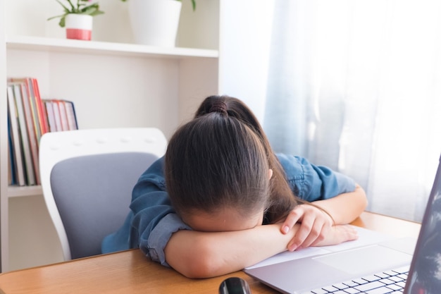 Teen girl brunette dressed in a denim shirt fell asleep at the workplace from fatigue doing homework