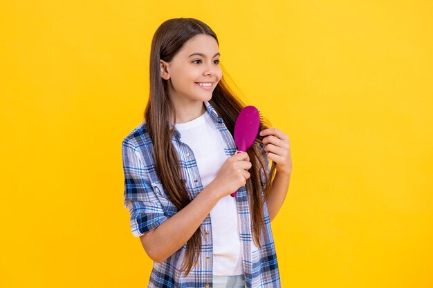 Teen girl brushing long hair with hairbrush pretty teen girl with hairbrush teen girl using a hairbrush to style her hair isolated on yellow teen girl holding hairbrush while brushing her hair