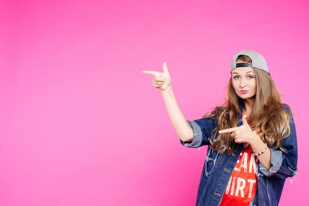 Teen girl in cap pointing at side and showing by fingers