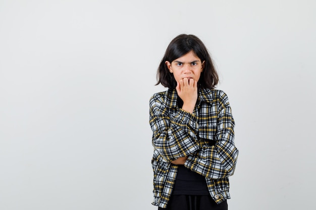 Ragazza teenager in camicia casual che morde le unghie e sembra stressata, vista frontale.