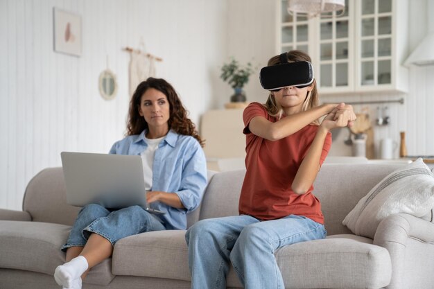 Foto ragazza adolescente con occhiali di realtà virtuale che gioca mentre sua madre lavora a distanza a casa