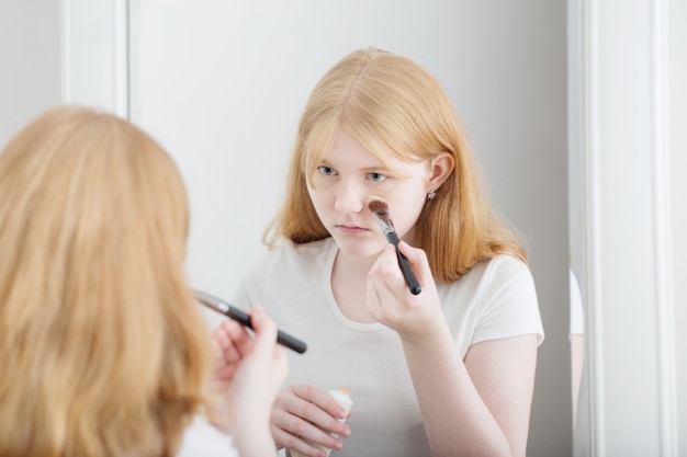 Teen girl examines acne on face in front of mirror