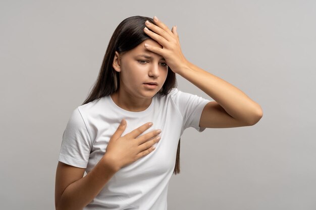 Photo teen girl feeling headache nausea touching chest forehead on gray background