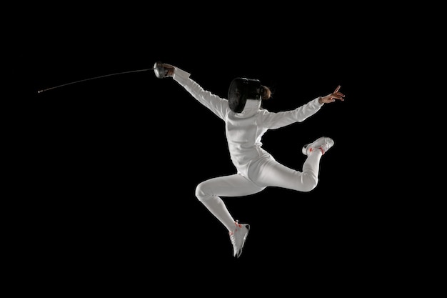 Photo teen girl in fencing costume with sword in hand isolated on black background