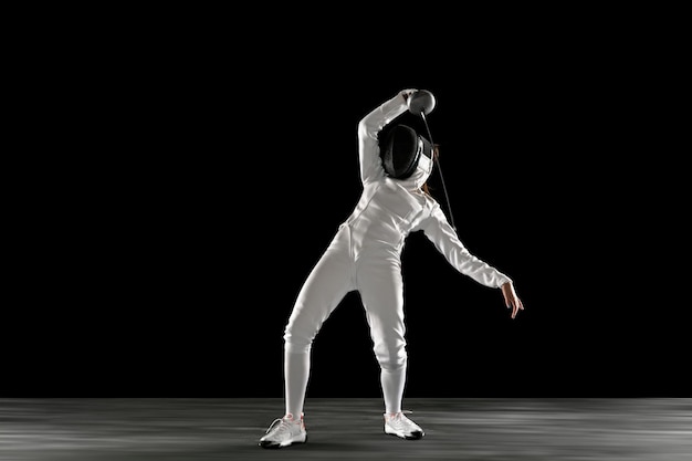 Teen girl in fencing costume with sword in hand isolated on black background