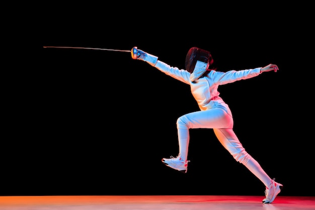 Teen girl in fencing costume with sword in hand isolated on black background