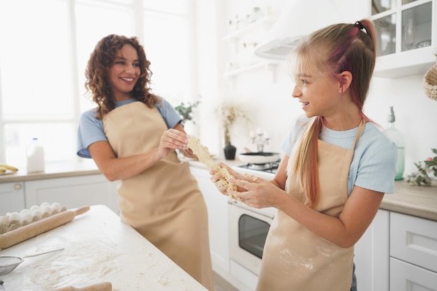 Photo teen girl helping her mom to cook dough in their kitchen at home