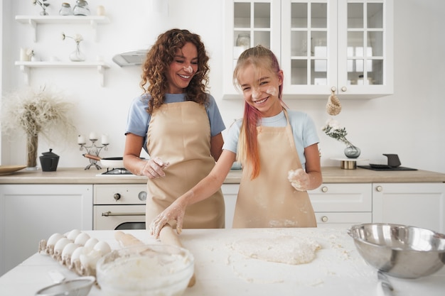 Teen girl helping her mom to cook dough in their kitchen at home