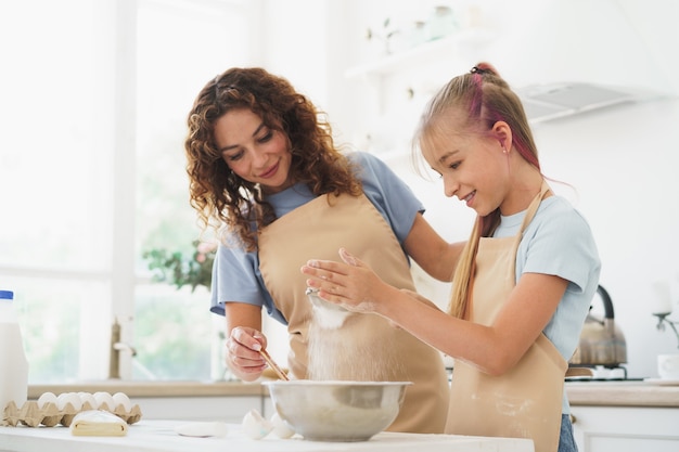 Teen girl helping her mom to cook dough in their kitchen at home