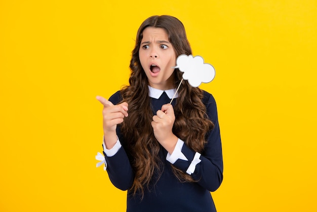 Teen girl holding clouds empty space thinking bubble comment cloud over yellow background Surprised