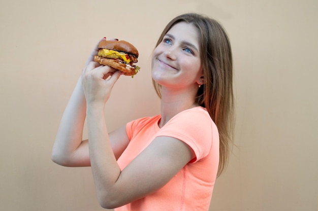 teen girl holds a big burger in her hand she smiles and smells a cheeseburger
