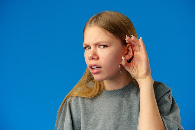 Teen girl holds her hand near her ear and listening something on blue background