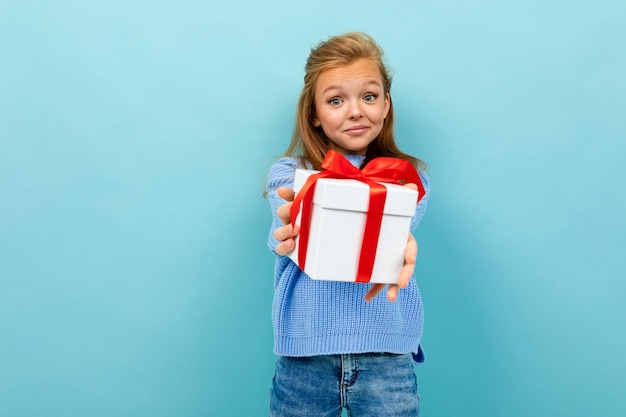 Photo teen girl holds out a gift with a red ribbon on a light blue