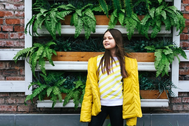 写真 黄色のジャケットと植物から生垣の背景にスウェットシャツの十代の少女