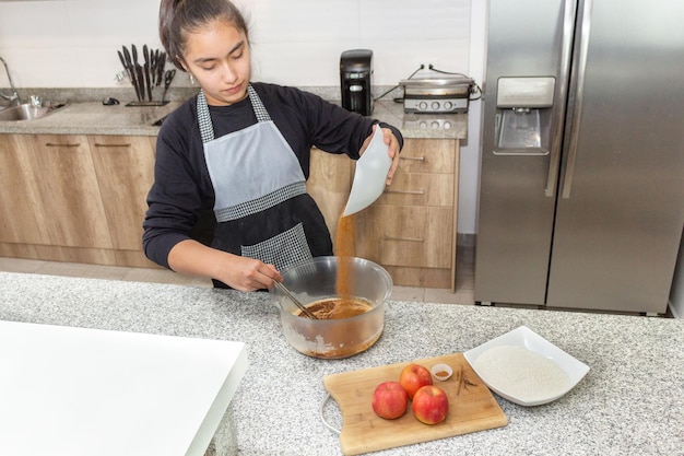 Teen girl incorporating chocolate into a cake dough in her home kitchen process for preparing an apple pie