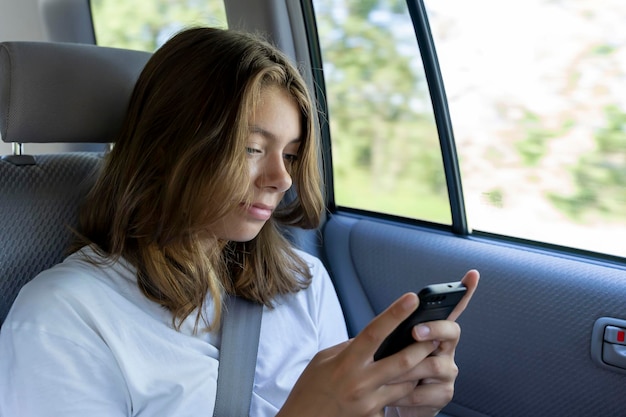 Photo teen girl is riding in the back seat of a car and uses smartphone