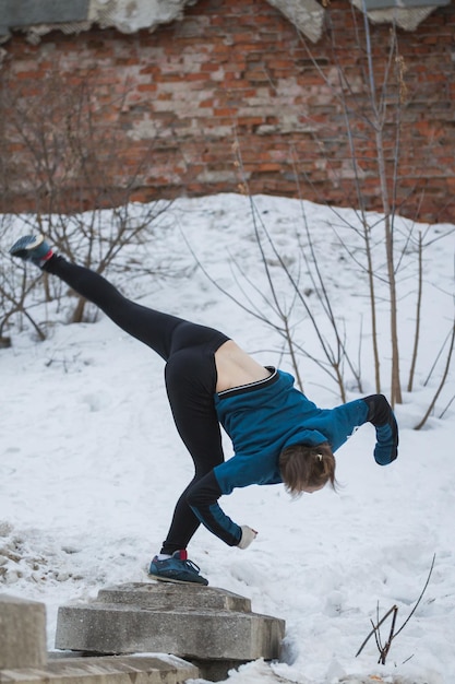 Teen girl jumping flip in snow winter park - free-run parkour concept, telephoto