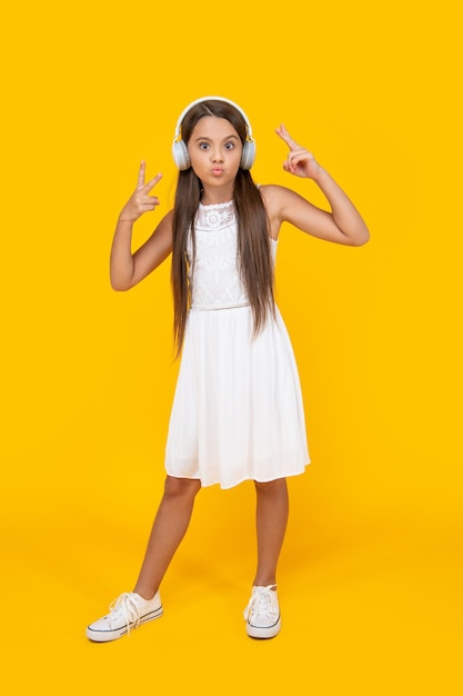 Teen girl listen music in headphones on yellow background peace