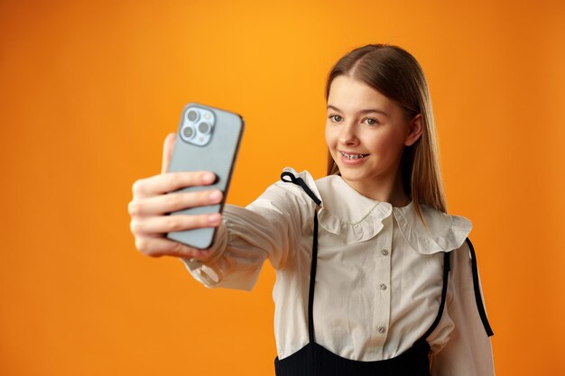 Teen girl making a selfie on her phone against yellow background