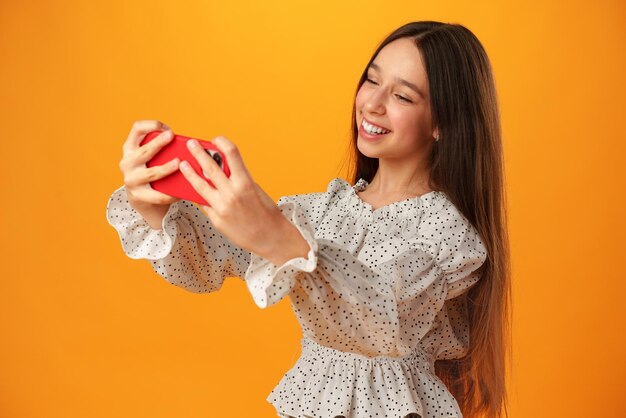 Teen girl making a selfie on her phone against yellow background