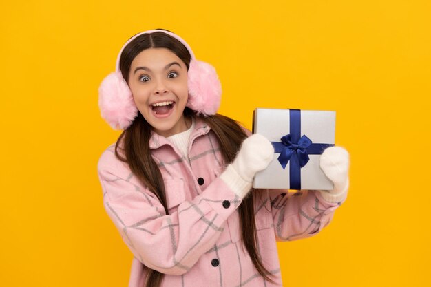 Teen girl in mittens hold present on yellow background xmas holiday gift