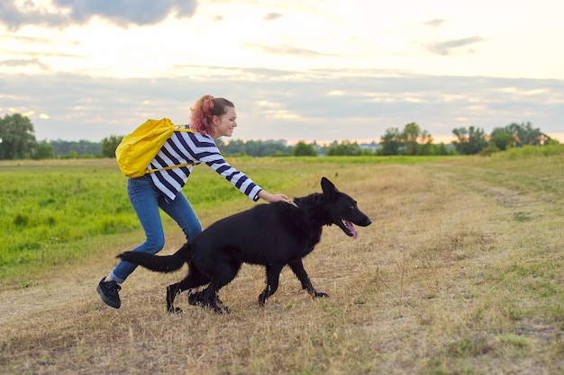 Teen girl pet owner playing and talking with big black shepherd dog