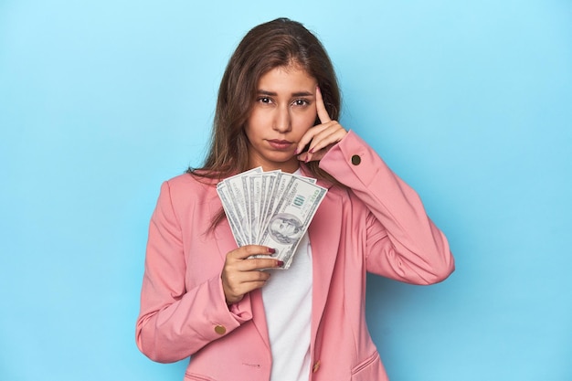 Teen girl in pink flaunting a handful of dollar bills showing a disappointment gesture