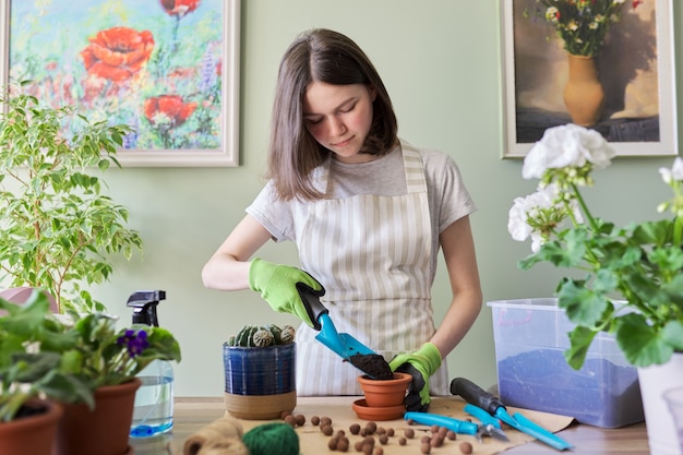 Photo teen girl plants small cactus in pot. hobbies and leisure, home gardening, houseplant, urban jungle in apartment, potted friends concept