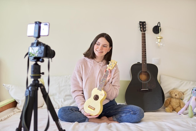 Teen girl playing on ukulele. Blog, music channel, vlog, girl studying online, talking to followers and playing music