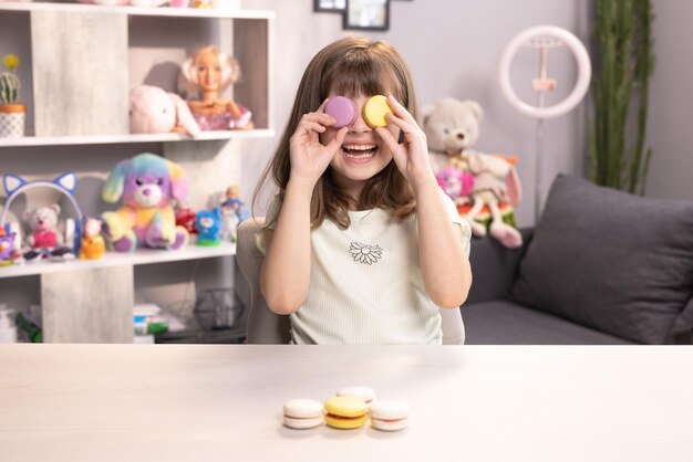 Teen girl plays with dessert macarons holding the cookies like glasses around the eyes