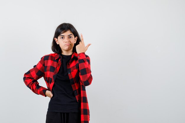 Teen girl pointing up in t-shirt, checkered shirt and looking careful , front view.