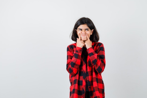 Ragazza teenager che preme le dita sulle fossette, guardando da parte in camicia casual e sembra curiosa. vista frontale.