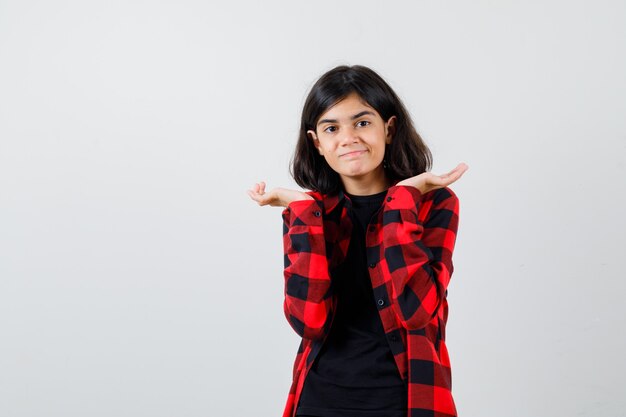 Teen girl pretending to hold something in t-shirt, checkered shirt and looking pleased , front view.