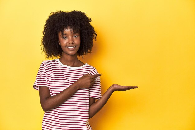 Photo teen girl in red striped tshirt yellow studio backdrop excited holding a copy space on palm