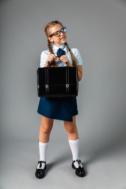 Teen girl in school uniform holding briefcase isolated on gray background