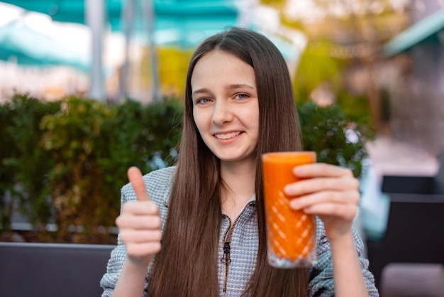 Photo teen girl show gesture like thumb up for pumpkin juice drinking in cafe